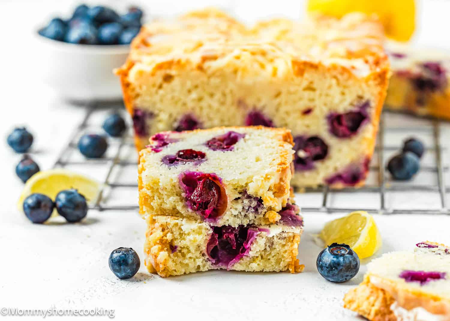 a slice of Eggless Lemon blueberry Loaf Cake cut in half with fresh blueberries and lemon wedges on the sides.