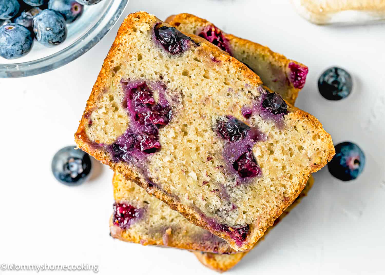two slices of Moist Blueberry Banana Bread without eggs over a white surface.