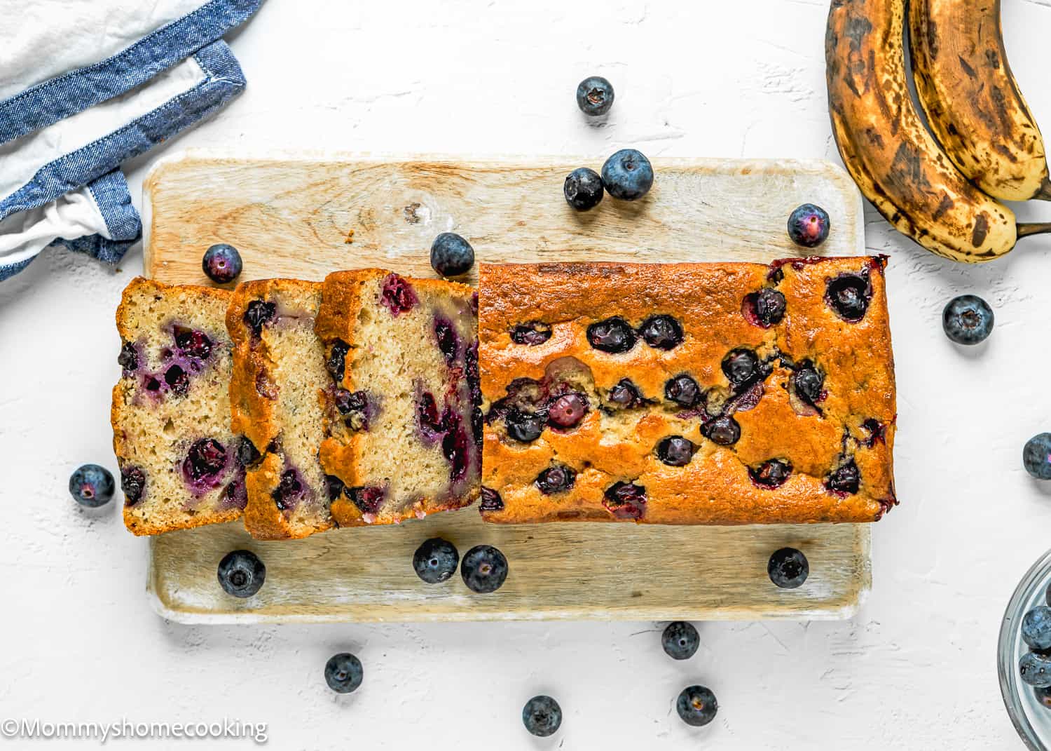 sliced Moist Blueberry Banana Bread without eggs over a wooden board with fresh blueberries and bananas around it.