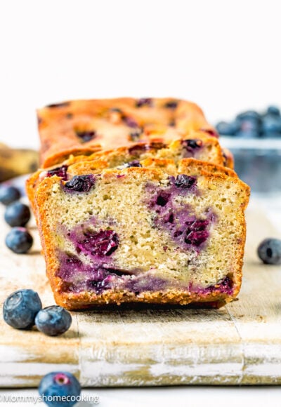 sliced Moist Blueberry Banana Bread without eggs over a wooden board with fresh blueberries around it.