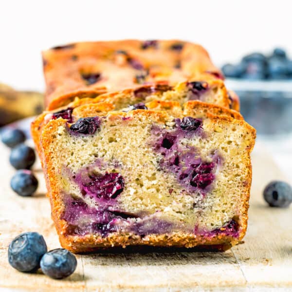 sliced Moist Blueberry Banana Bread without eggs over a wooden board with fresh blueberries around it.