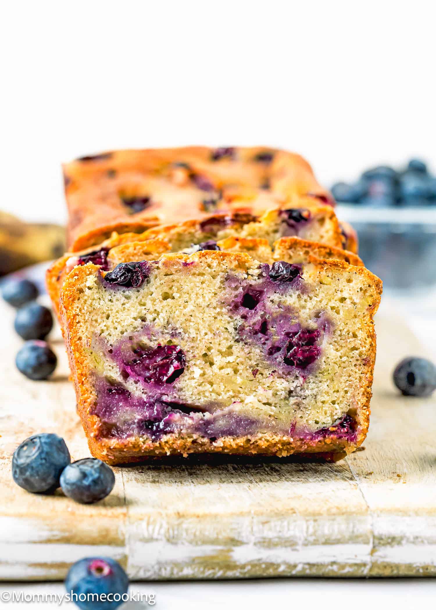sliced Moist Blueberry Banana Bread without eggs over a wooden board with fresh blueberries around it.