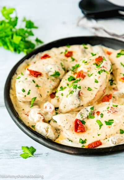 One Pan Creamy Chicken and Mushrooms garnished with chopped Parsley over a blue surface with serving spoons in the background.