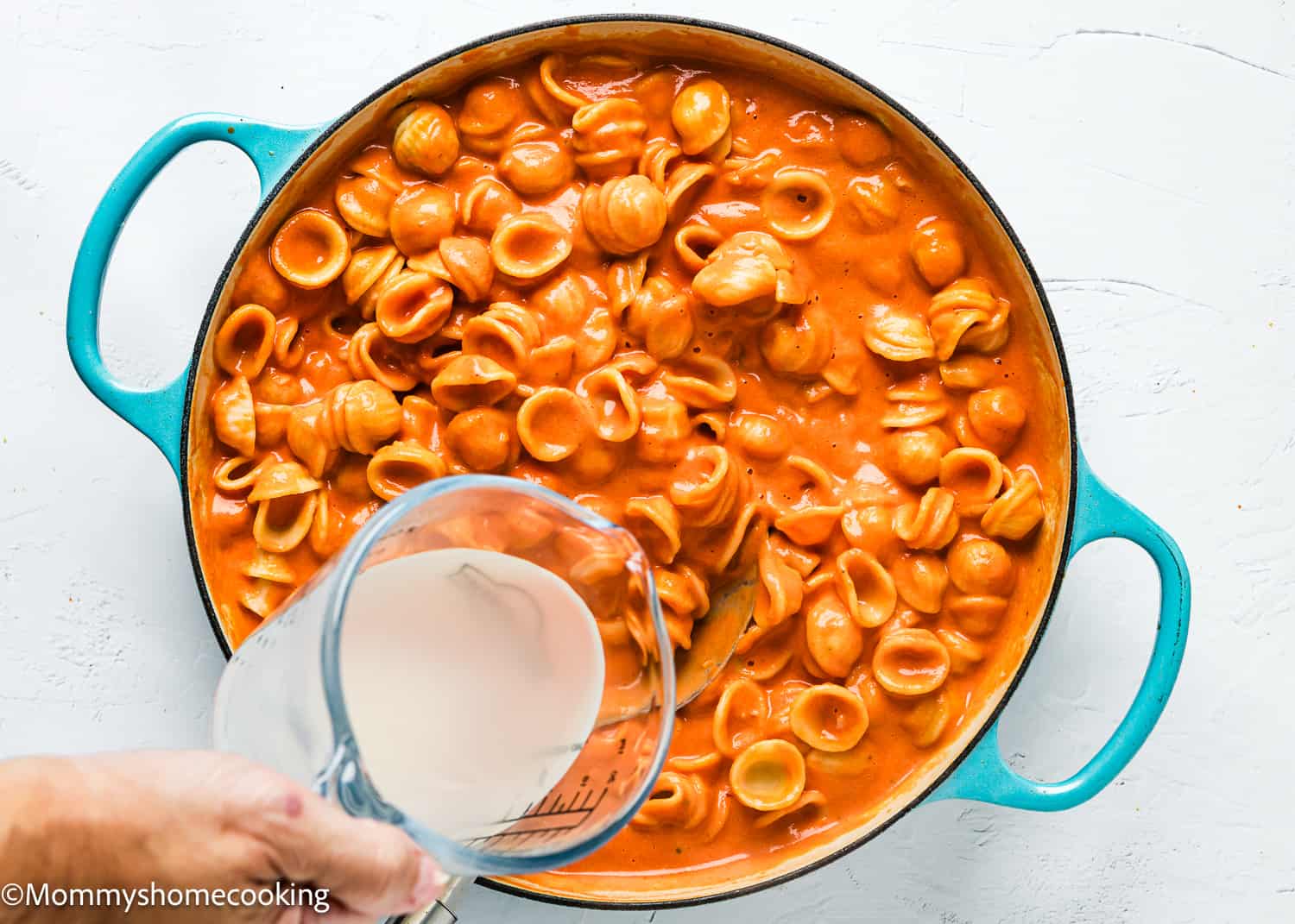 a hand pouring pasta cooking water to a skillet with creamy tomato pasta.