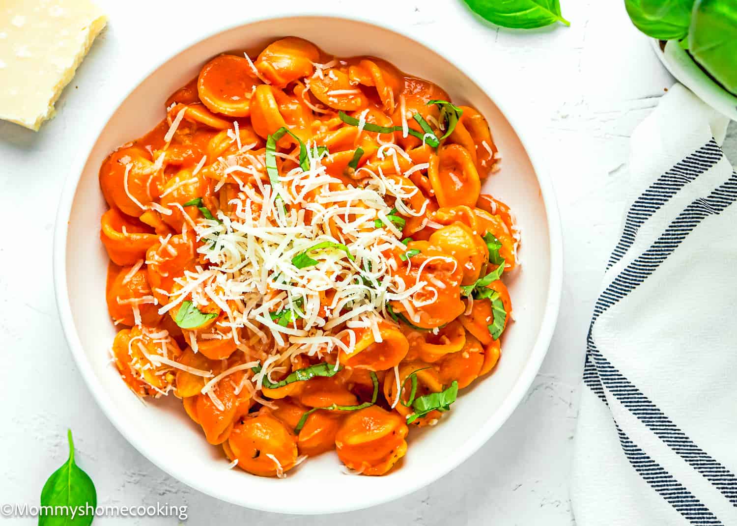 Creamy Tomato Pasta in a plate with grated cheese and basil on a white surface.
