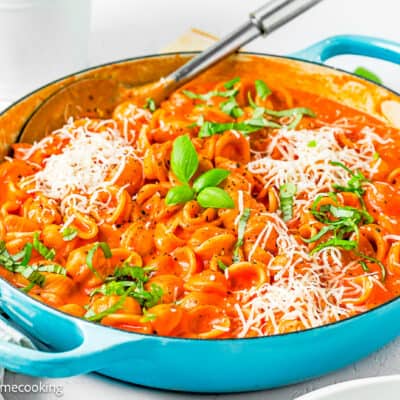 Creamy Tomato Pasta in a blue skillet with a serving spoon, grated cheese and basil.