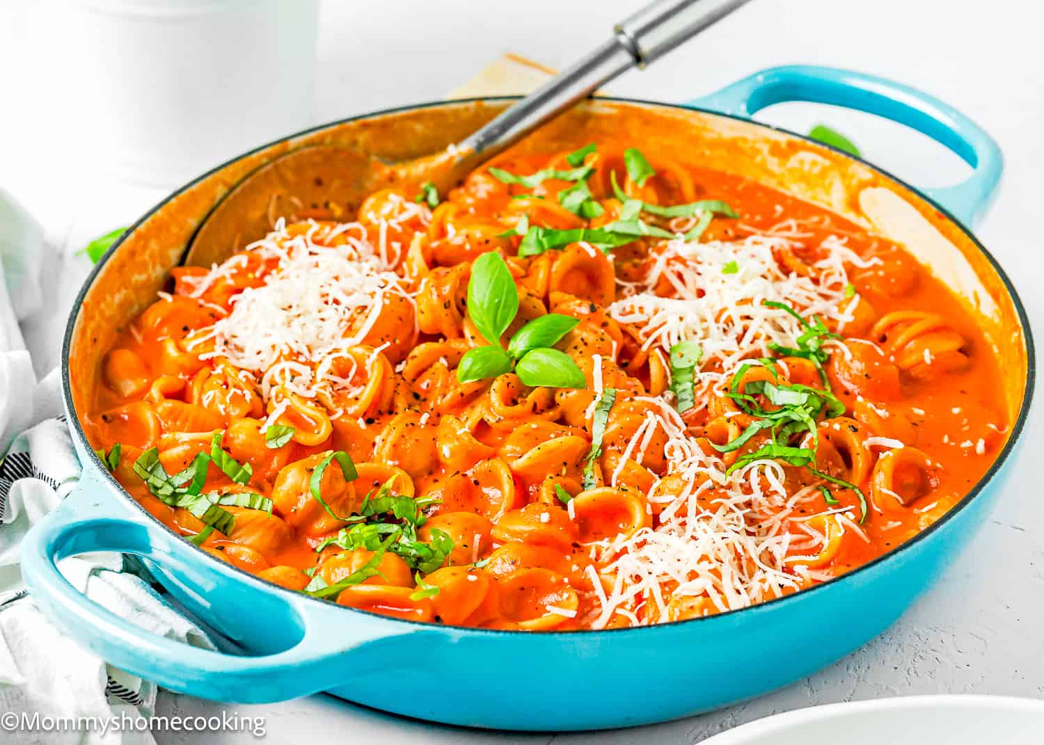 Creamy Tomato Pasta in a blue skillet with a serving spoon, grated cheese and basil.