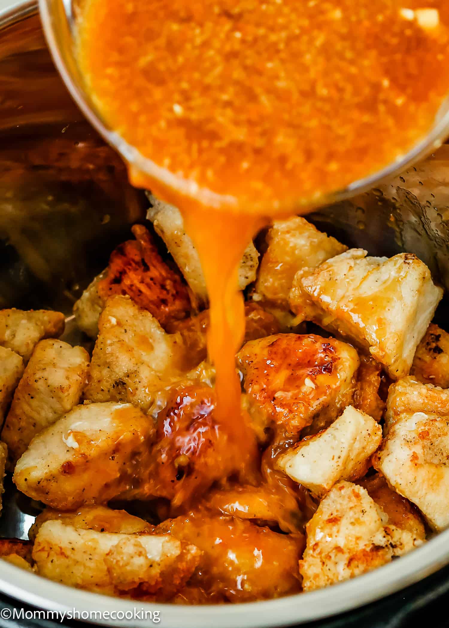 orange sauce being poured over cooked chicken to make homemade orange chicken. 