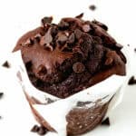 a whole Bakery-Style egg-free and dairy-free Double Chocolate Muffin over a white surface with chocolate chips around it.