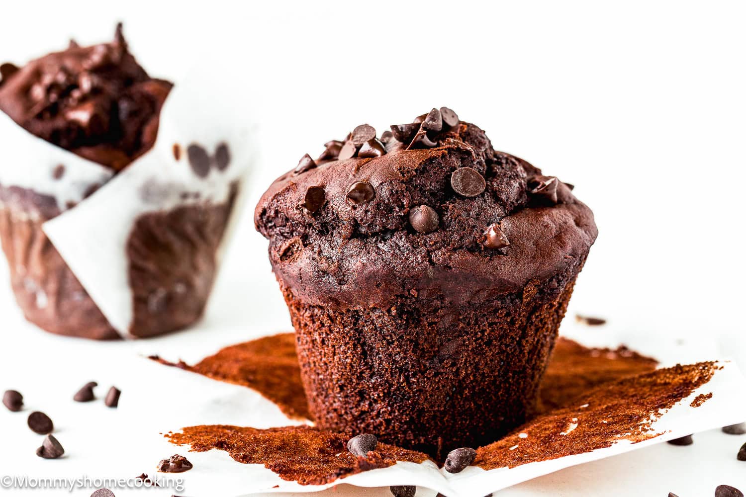 a whole Bakery-Style egg- free and dairy-free Double Chocolate Muffin over a white surface with another muffins in the background.