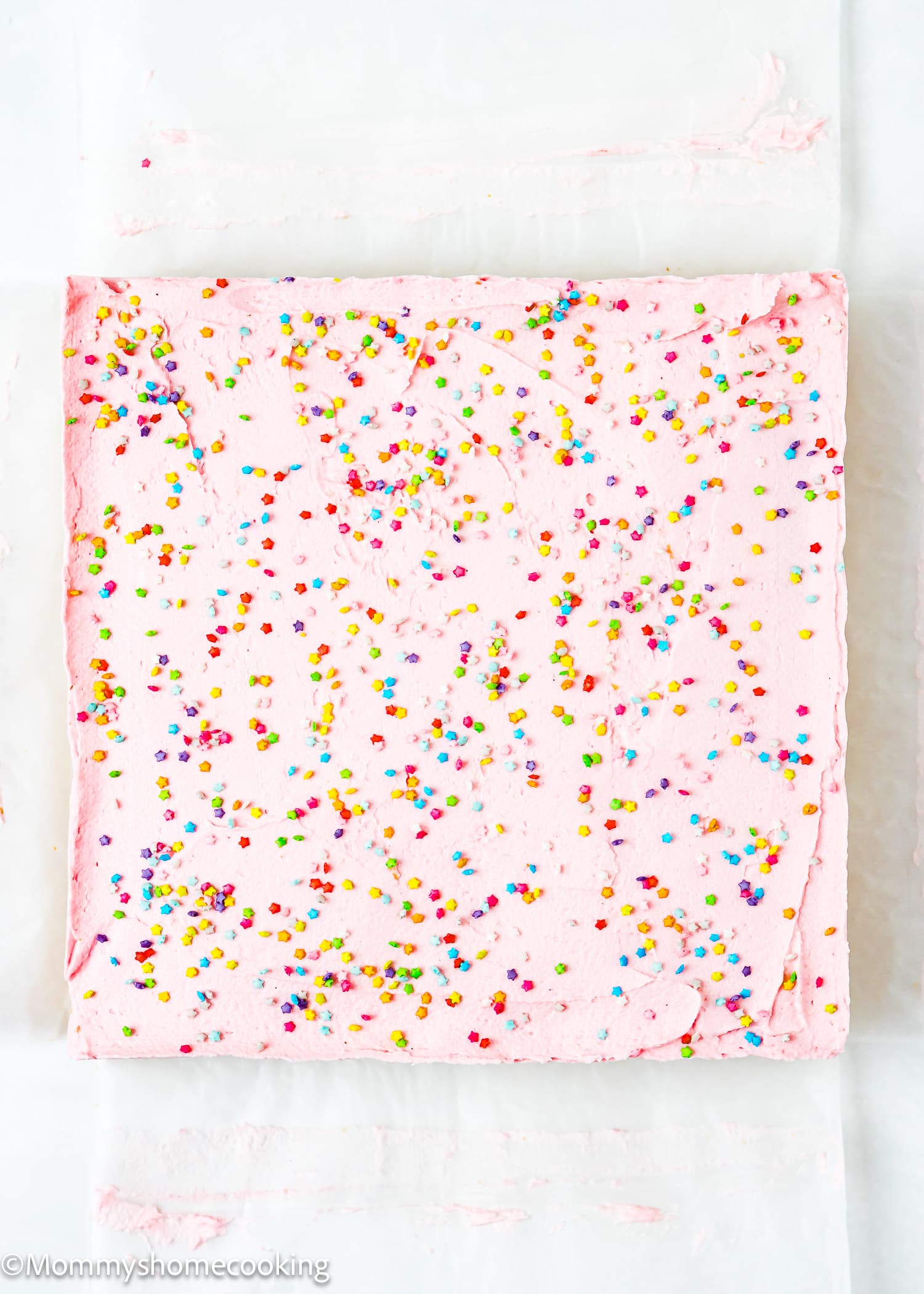 a whole slab of Eggless Sugar Cookie Bars with frosting and sprinkles over parchment paper.