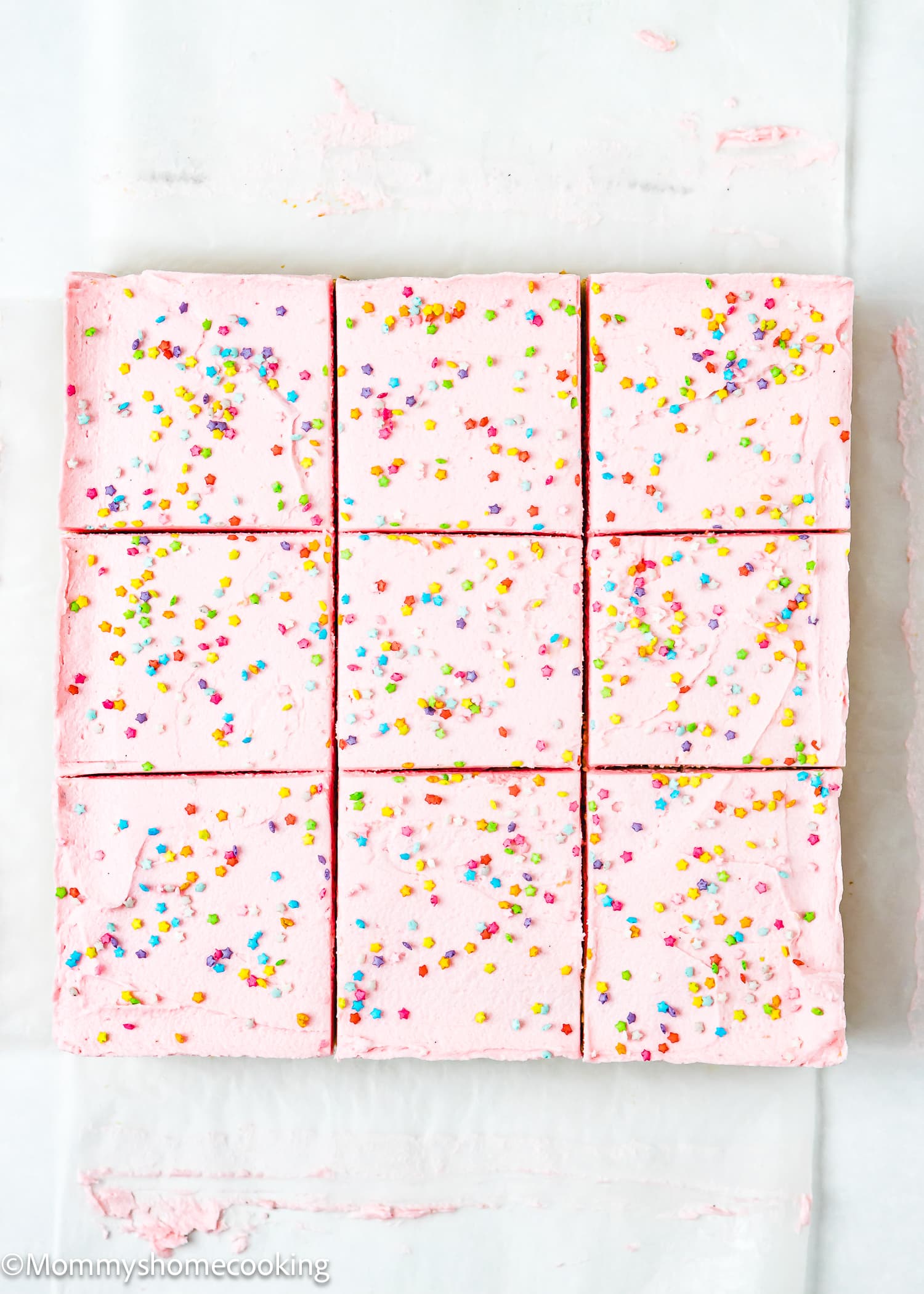 Nine Eggless Sugar Cookie Bars with frosting and sprinkles over parchment paper.