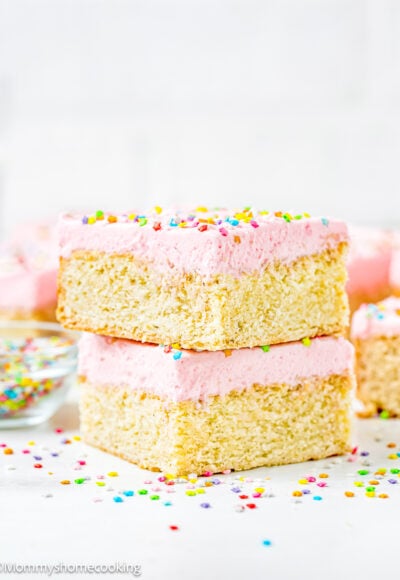 two Eggless Sugar Cookie Bars with frosting and sprinkles over a white surface.