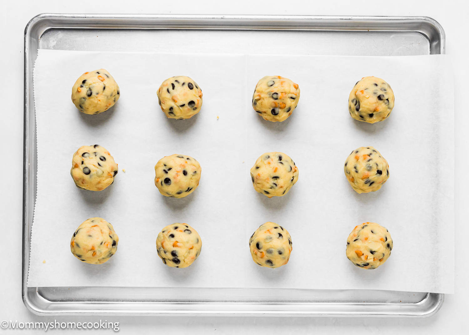 Unbaked eggless Butterscotch Chocolate Chip Cookie balls on a baking tray.