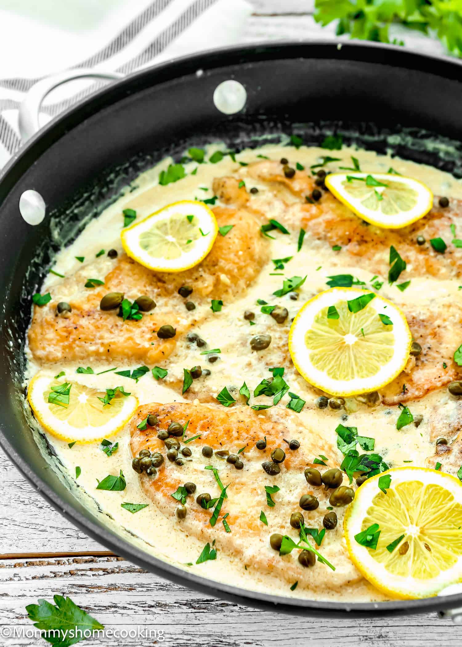 Easy Chicken Piccata in creamy sauce with lemon slices and capers with a kitchen towel in the background.