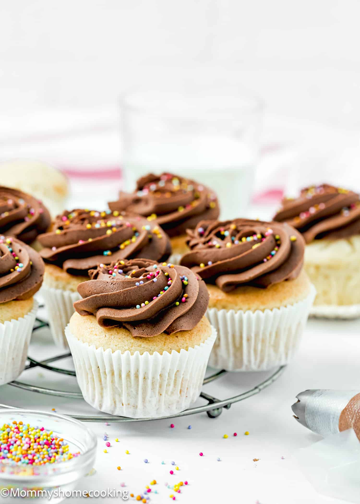 Easy Fluffy Vanilla Cupcake (Dairy-Free, Egg-Free, Vegan) with chocolate frosting and sprinkles over a cooling rack.