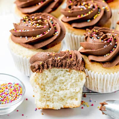 Easy Fluffy Vanilla Cupcakes (Dairy-Free, Egg-Free, Vegan) cut into half showing its inside texture with chocolate frosting and sprinkles with more cupcakes on the sides.