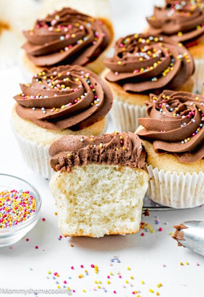 Easy Fluffy Vanilla Cupcakes (Dairy-Free, Egg-Free, Vegan) cut into half showing its inside texture with chocolate frosting and sprinkles with more cupcakes on the sides.