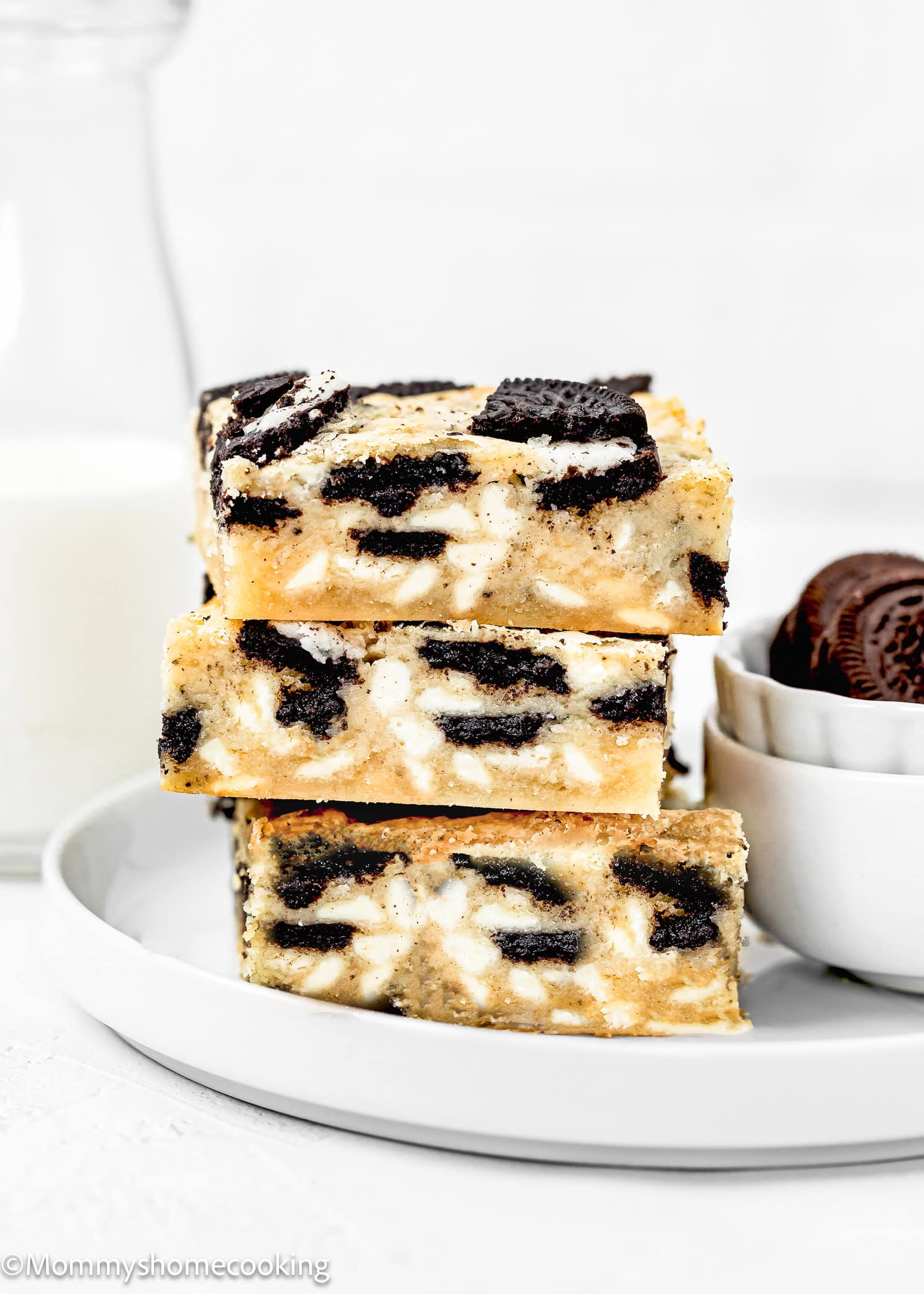Stack of three Easy Oreo Blondies (Egg-Free) on a plate with two bowl on the side and a milk bottle in the background.