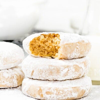 stack of three Eggless Old Fashioned Powdered Sugar Donuts showing its inside perfect texture with more donuts around it.