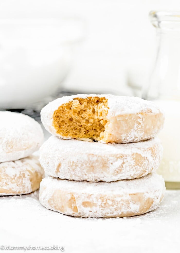 stack of three Eggless Old Fashioned Powdered Sugar Donuts showing its inside perfect texture with more donuts around it.