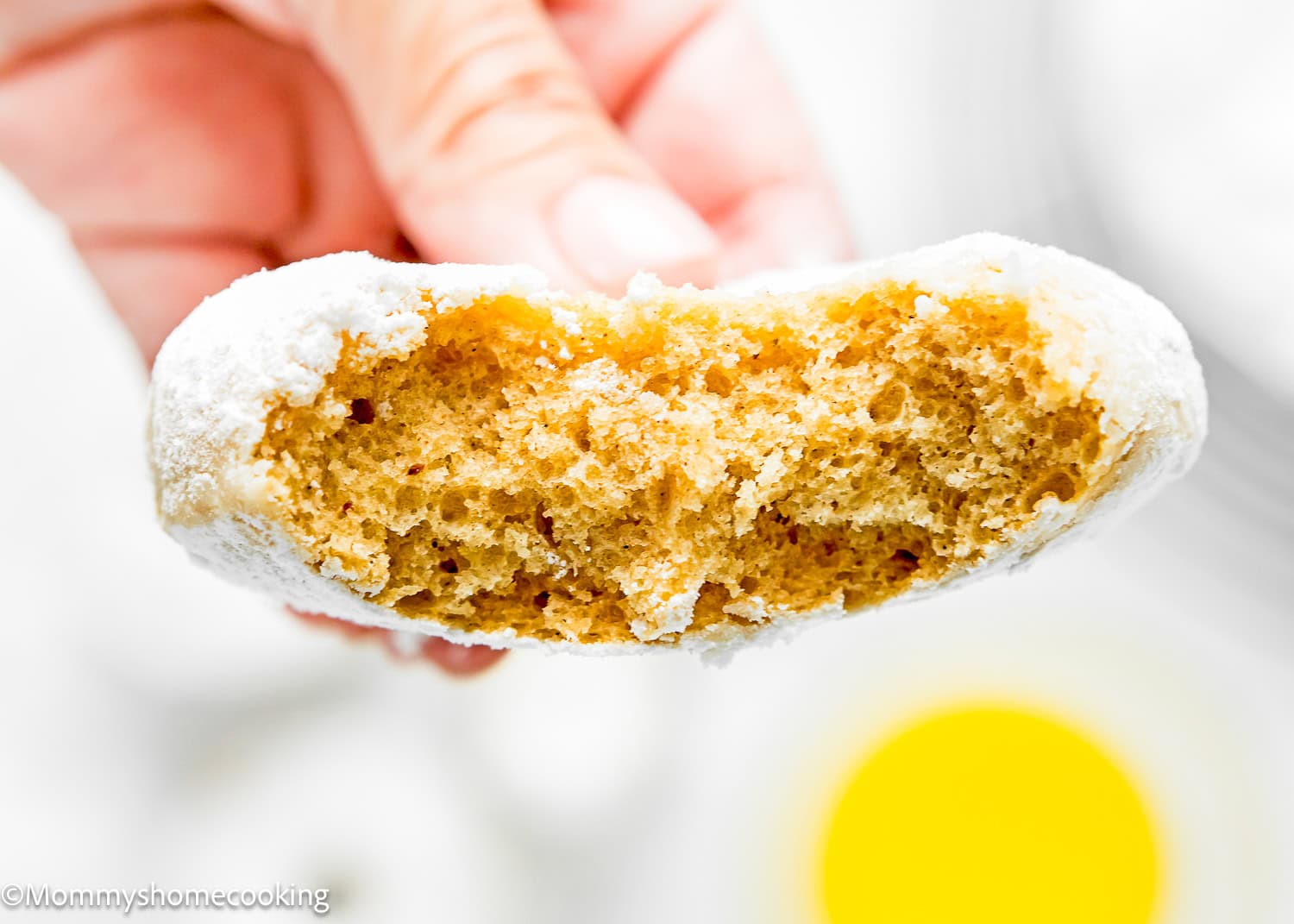 a woman hand holding aEggless Old Fashioned Powdered Sugar Donut showing its inside fluffy texture.