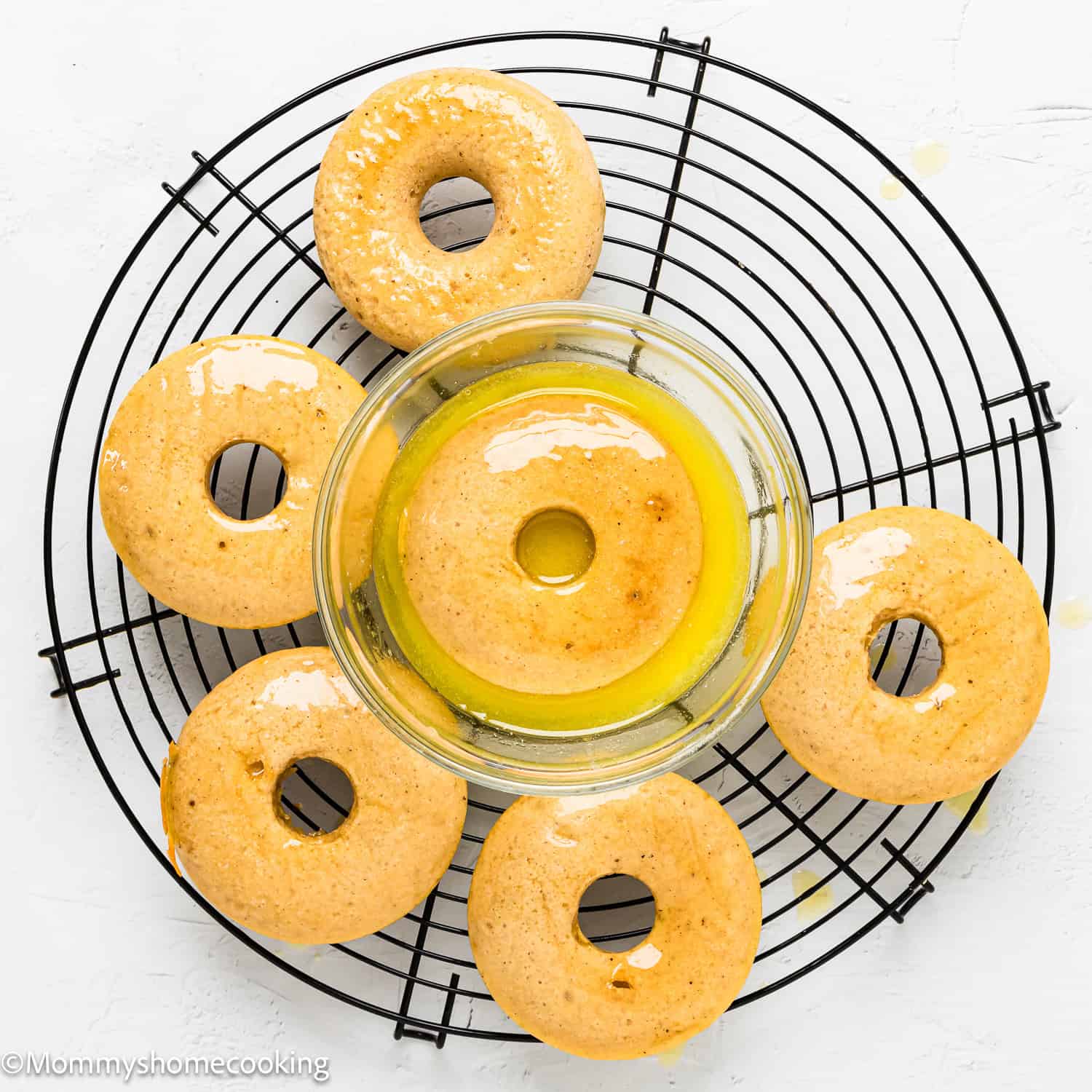 Eggless Donuts being dipped in butter over a cooling rack.