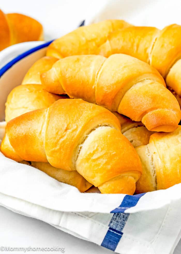 Homemade Eggless Crescents Rolls in a bread basket with a kitchen towel.