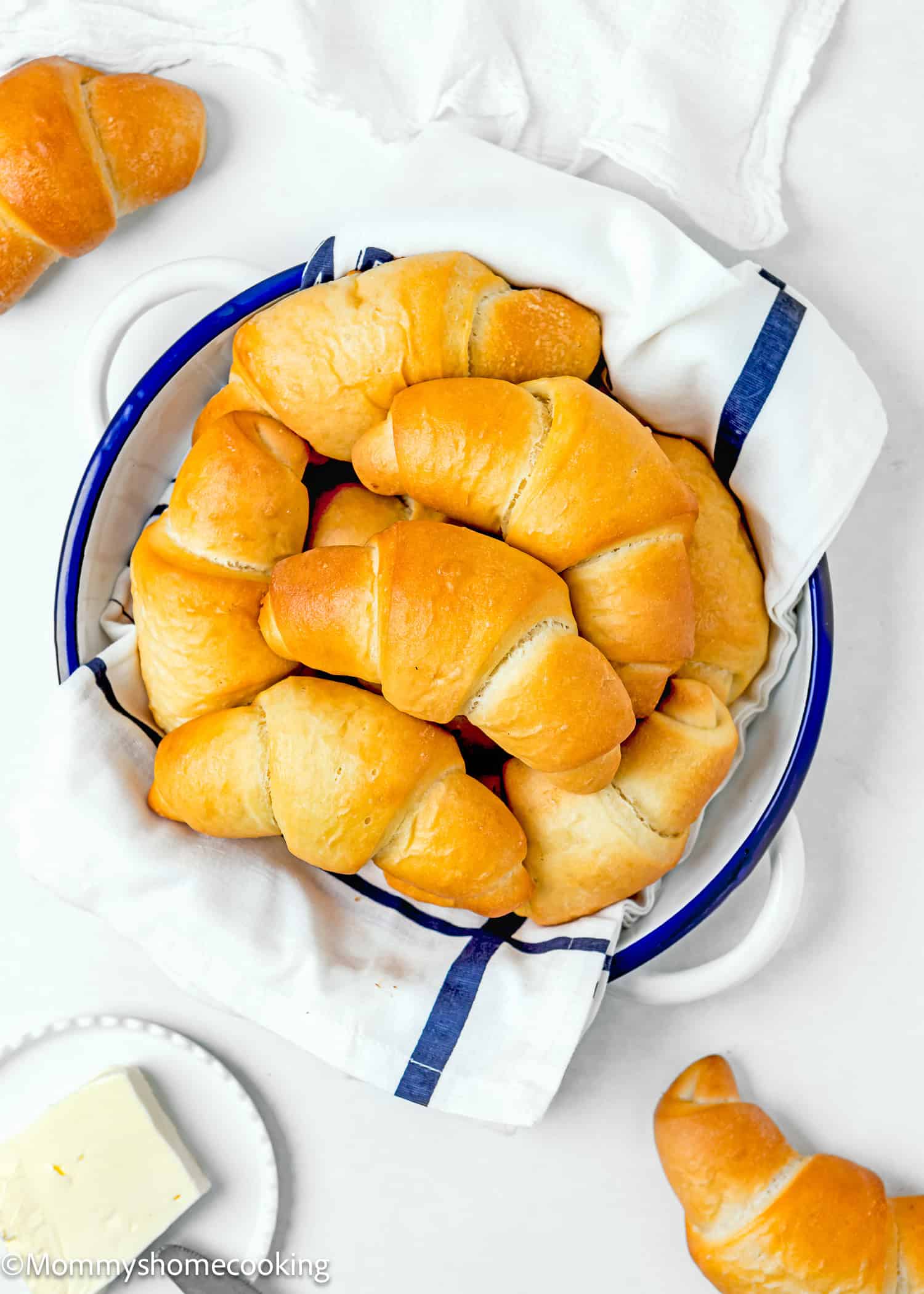 Homemade Eggless Crescents Rolls in a bread basket with a kitchen towel with more rolls around it over a white surface.