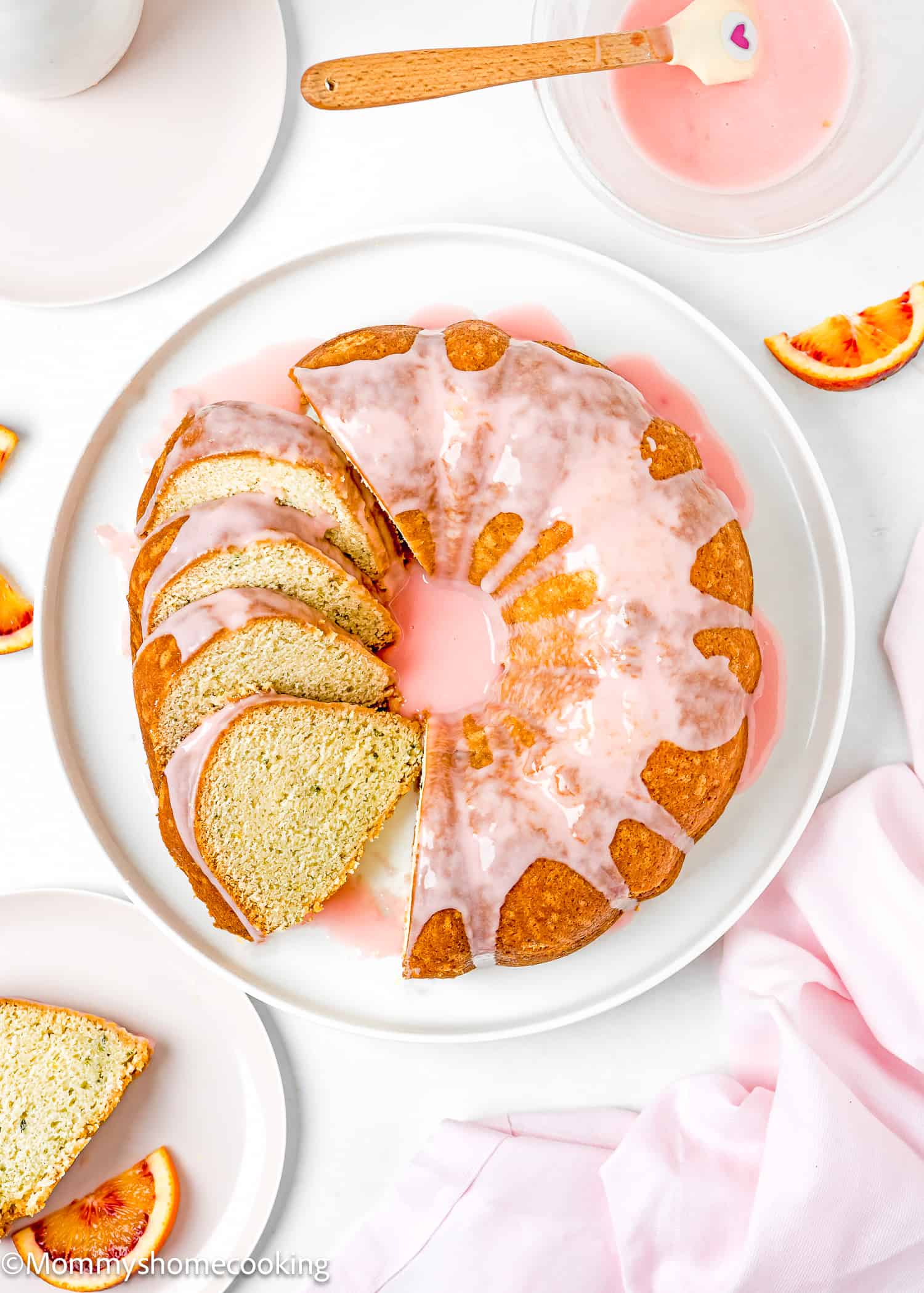 a sliced Simple Orange Bundt Cake without eggs with glaze on a serving plate with a plate and a bowl with orange glaze on the side.