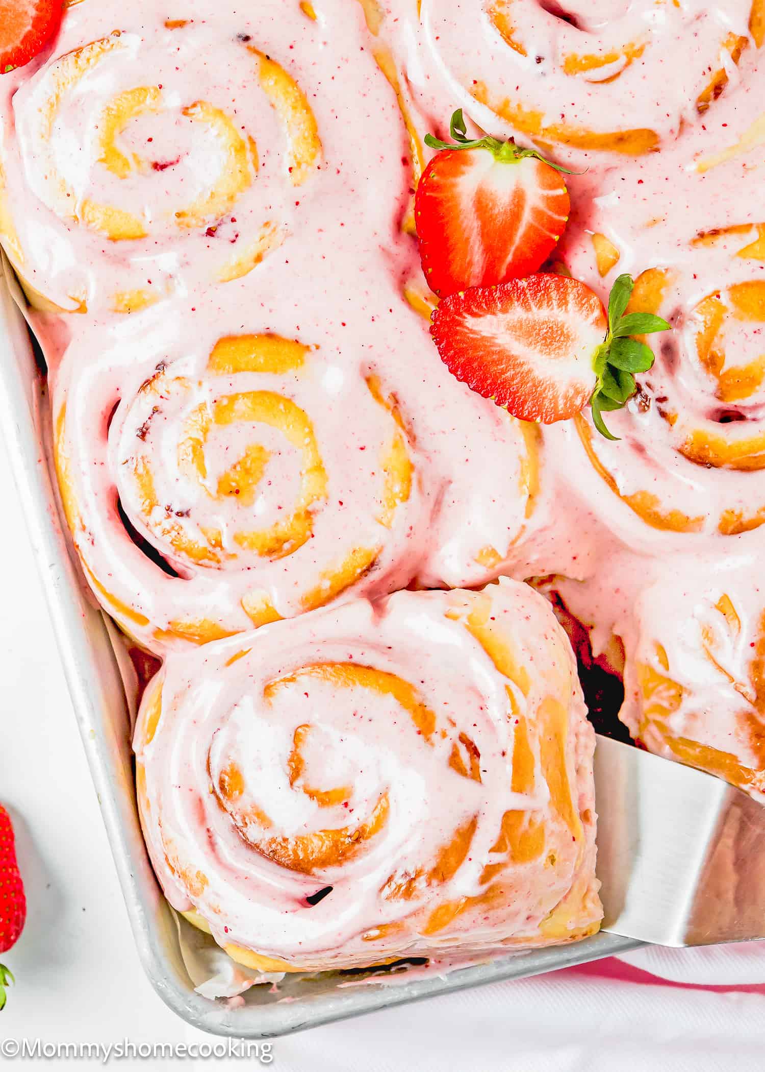 a spatula picking a Easy Strawberry Rolls with frosting from a baking pan.