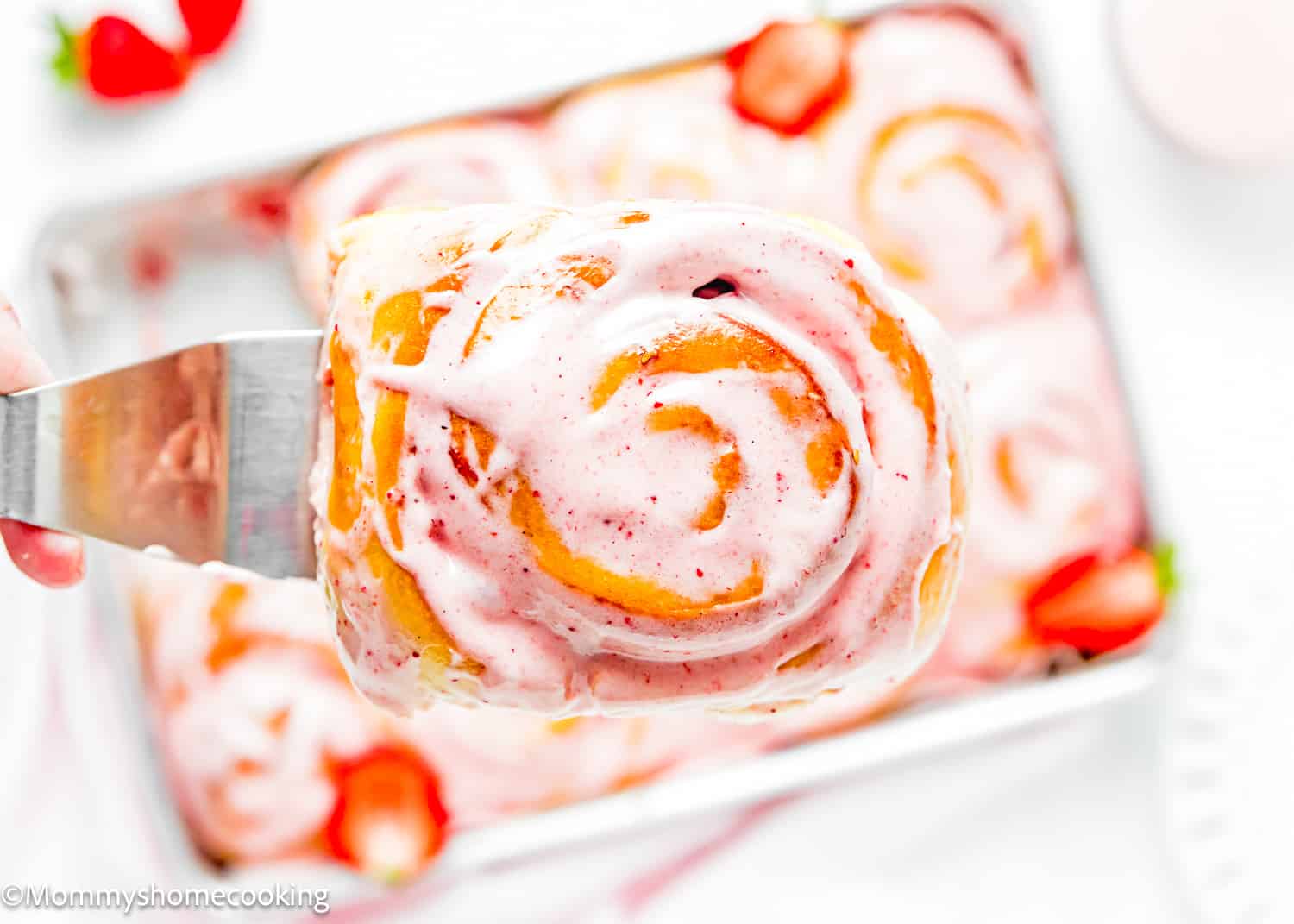 a spatula holding a Easy Strawberry Rolls with frosting.