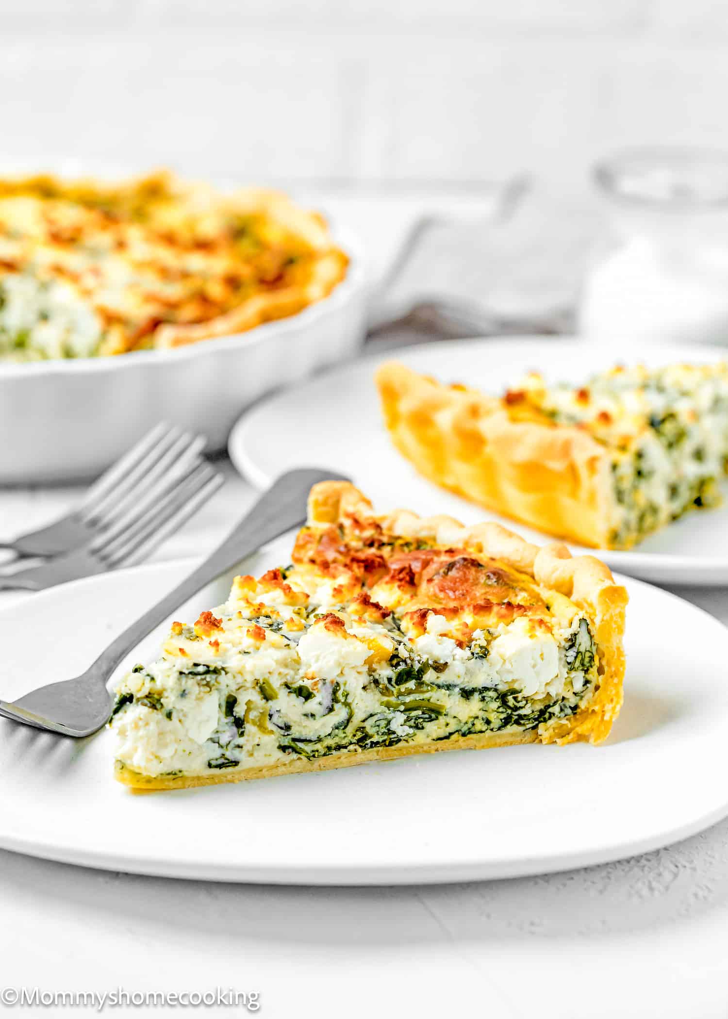 a slice of eggless quiche over a white plate with plates and forks on the sides.