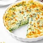 a sliced eggless quiche over a white surface with plates and forks on the sides.