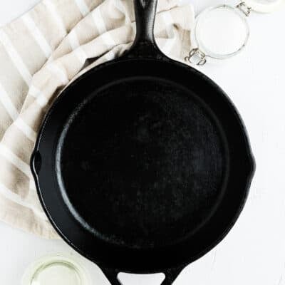 a cast iron pan with a containers with oil and side on the side and a kitchen towel.