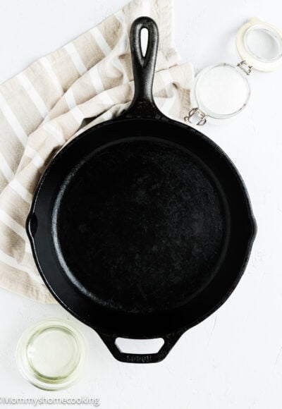 a cast iron pan with a containers with oil and side on the side and a kitchen towel.