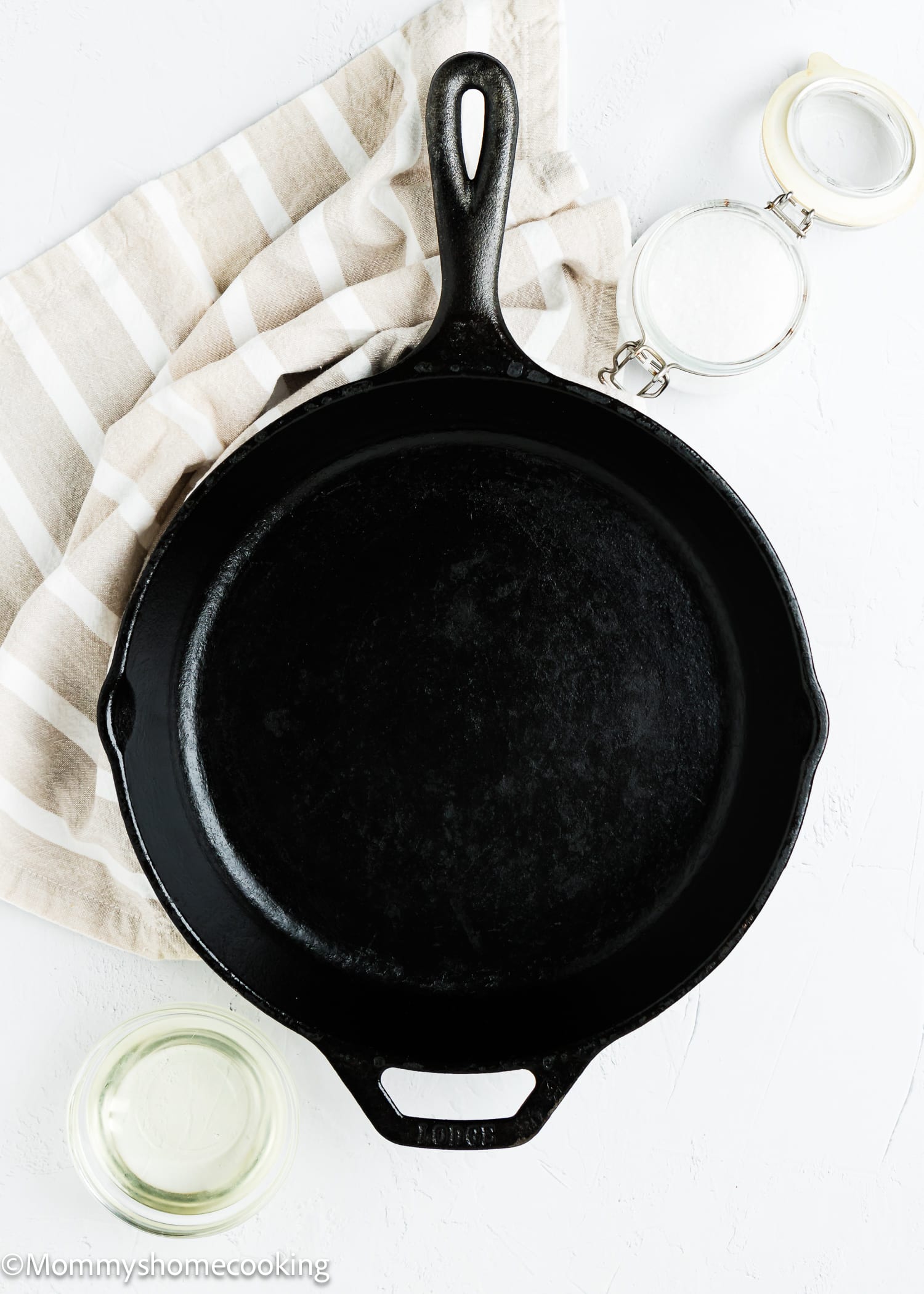 a cast iron pan with a containers with oil and side on the side and a kitchen towel. 