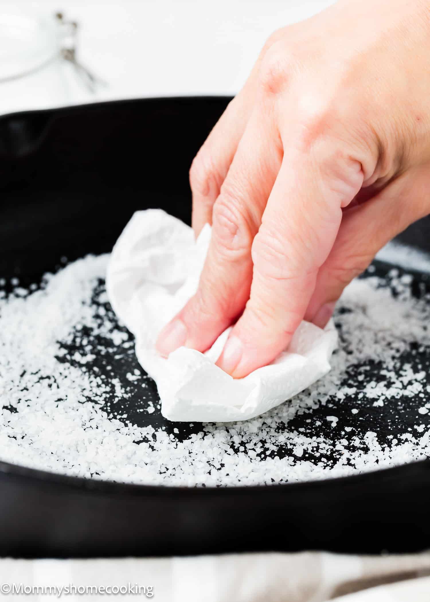 a woman hand scrubbing a cast iron pan with salt.