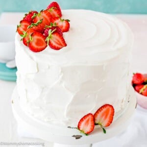 eggless strawberry shortcake cake decorated with Easy Whipped Cream Frosting and fresh strawberries on a cake stand.