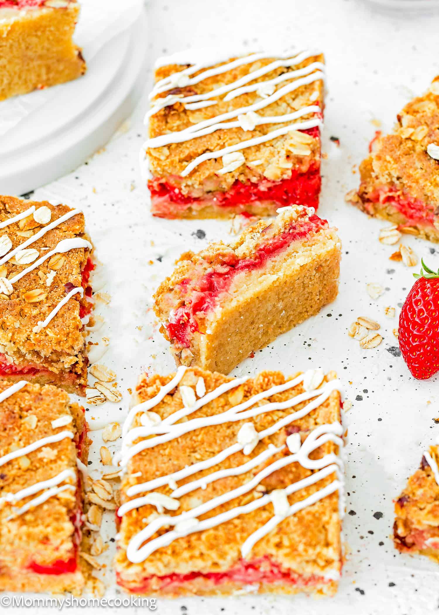 Egg-free Strawberry oat Bars over a white surface with fresh strawberries on the side.