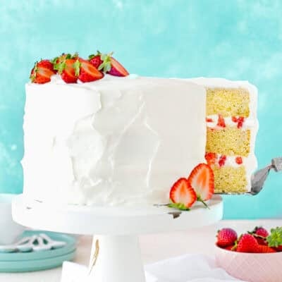 a cake server picking a slice of a Eggless Strawberry Shortcake Cake on a cake stand over a white surface.