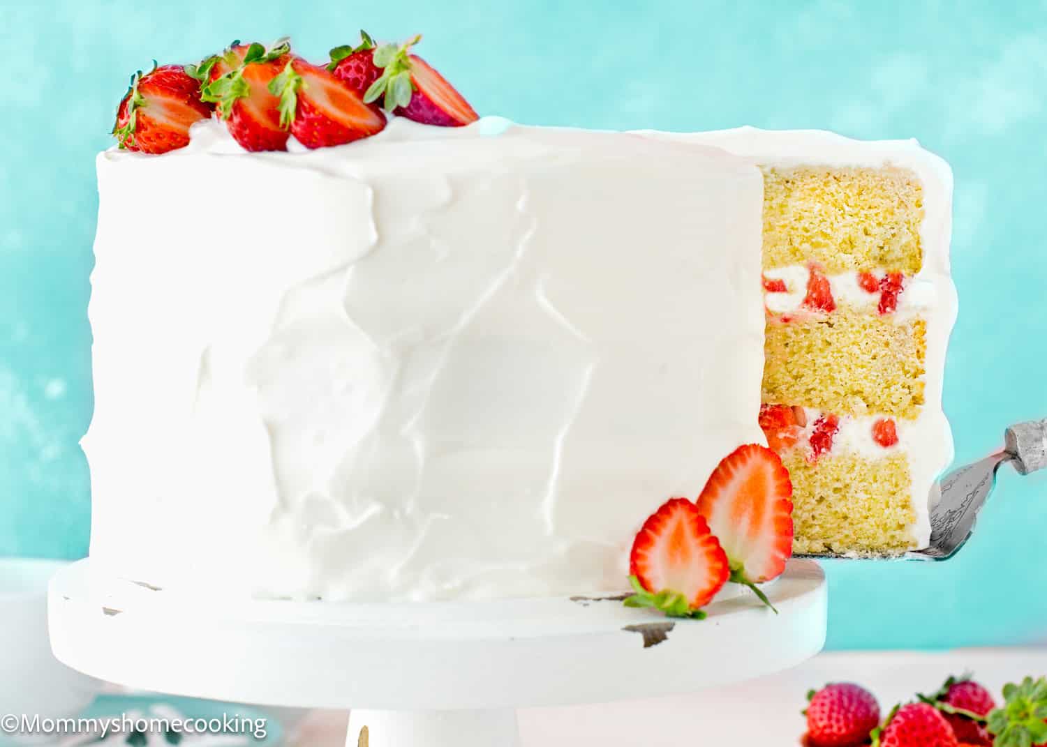 a cake server picking a slice of a Eggless Strawberry Shortcake Cake on a cake stand.