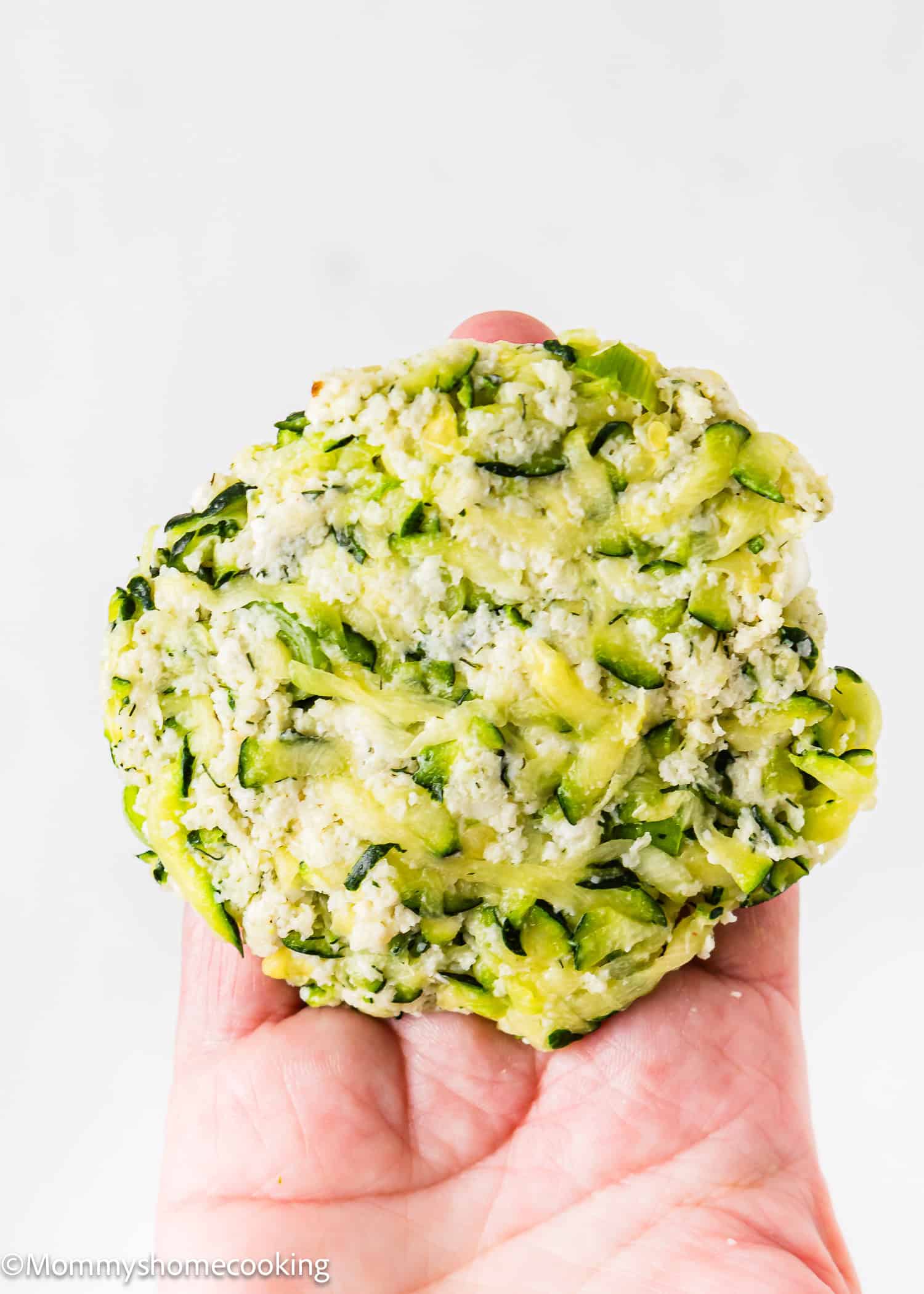 a woman hand holding a un cooked Eggless Zucchini Fritter pattie.