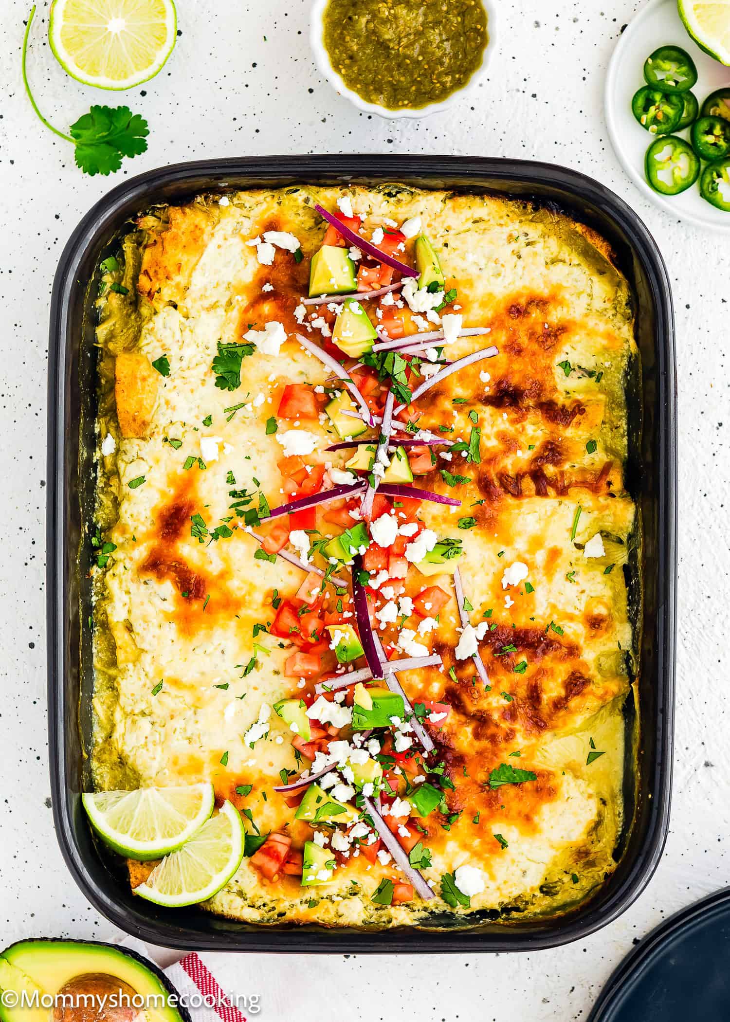Quick and Easy Enchiladas Suizas with topping in a black casserole dish over a white surface.