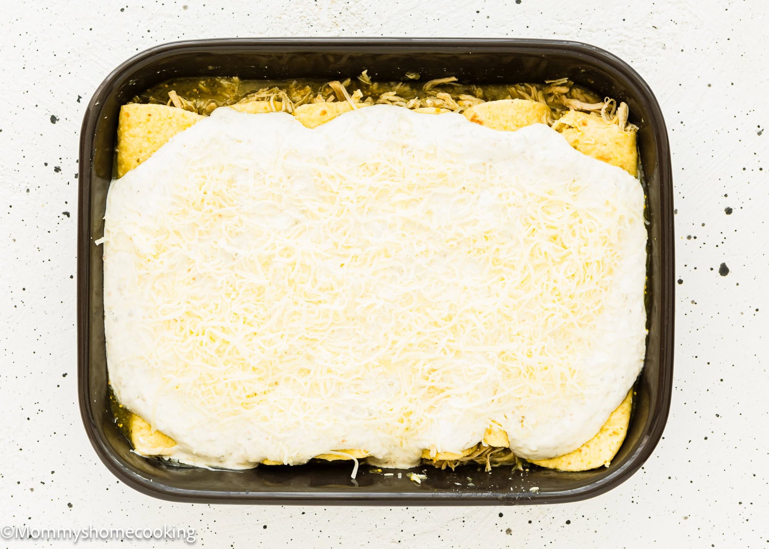 unbaked Enchiladas Suizas in a casserole dish with cream and cheese on top.