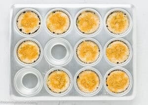 A 12-cup muffin tin with 10 unbaked Eggless Zucchini Muffins topped with breadcrumbs in paper liners, ready to go into the oven. Two cups are empty.