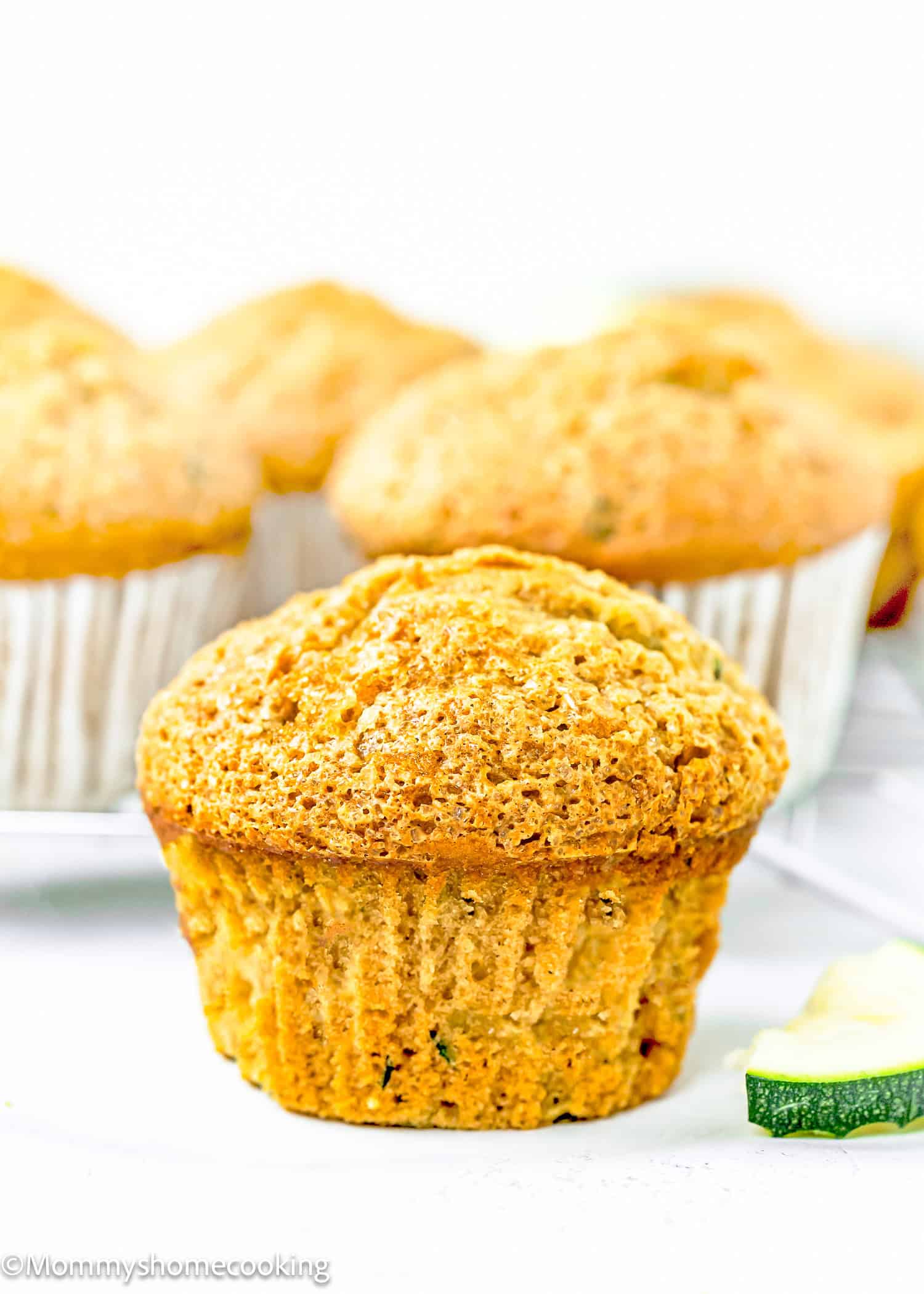 a Simple Vegan Zucchini Muffin over a white surface with more muffins in the background.