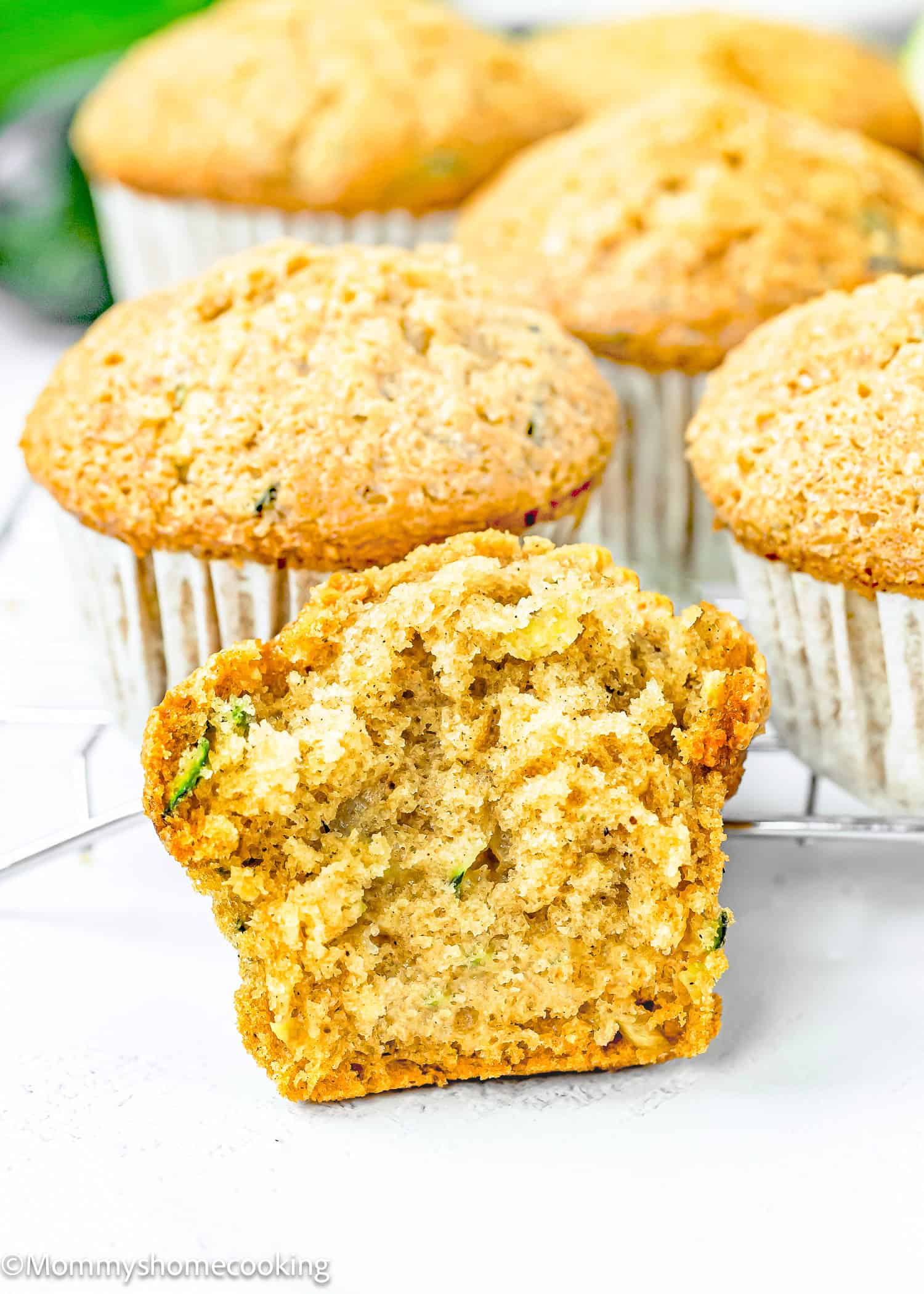 a Simple Vegan Zucchini Muffin cut in half over a white surface with more muffins in the background.