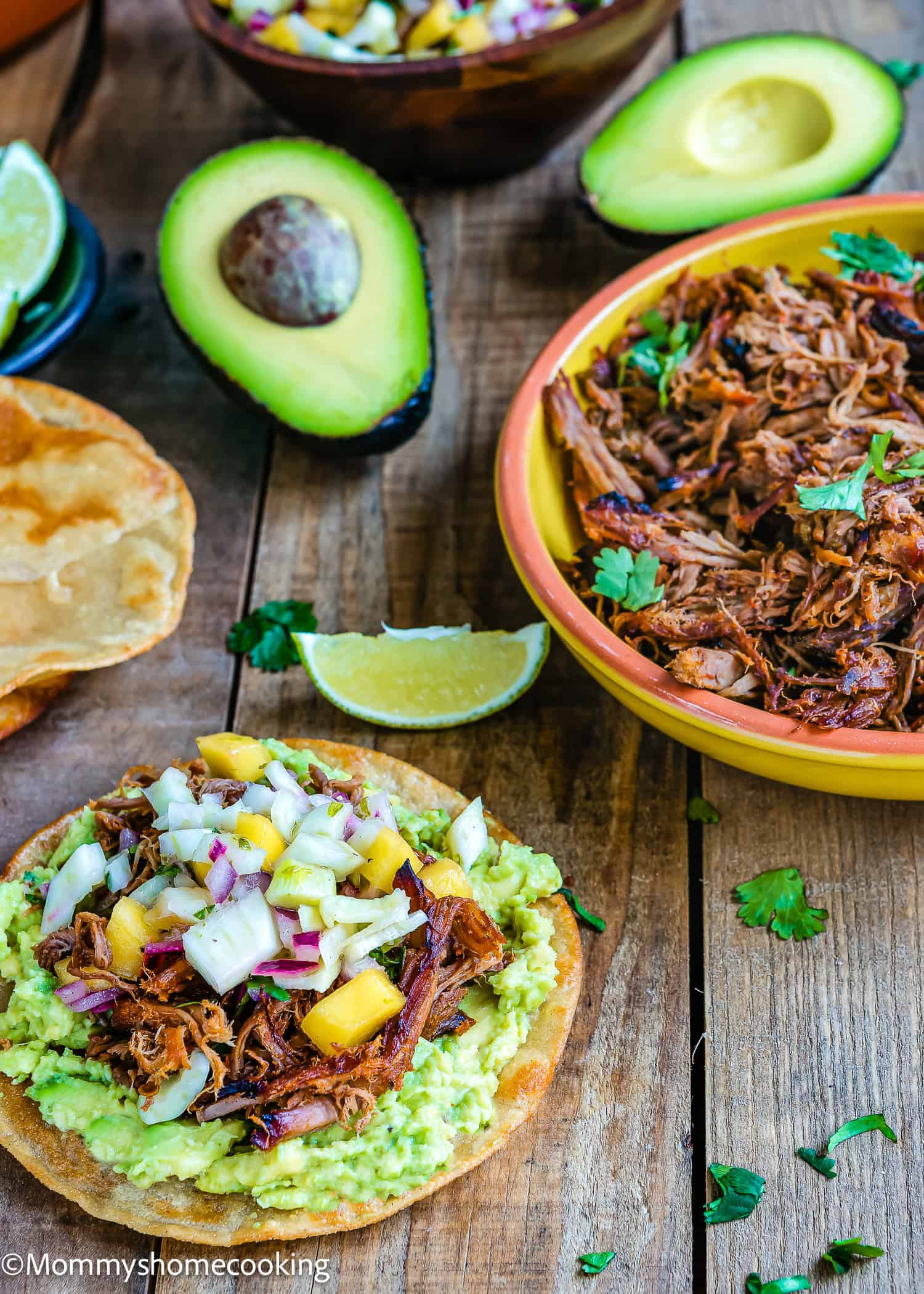 A Slow-Cooker Spicy Pork Carnitas tostada with mango salsa over a wooden surface. i