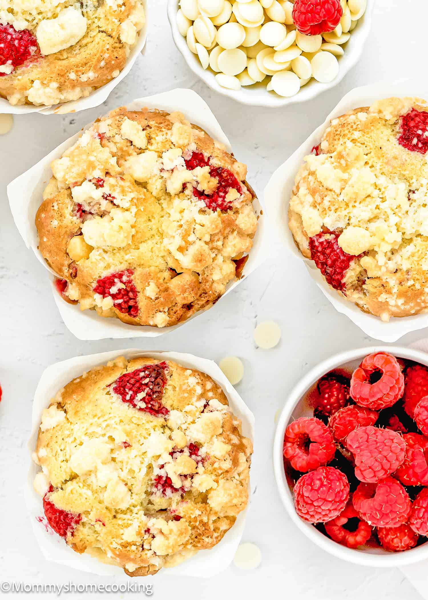 overhead view of Easy Vegan Raspberry Muffins with tulip liners over a white surface and a bowl with of fresh raspberries.
